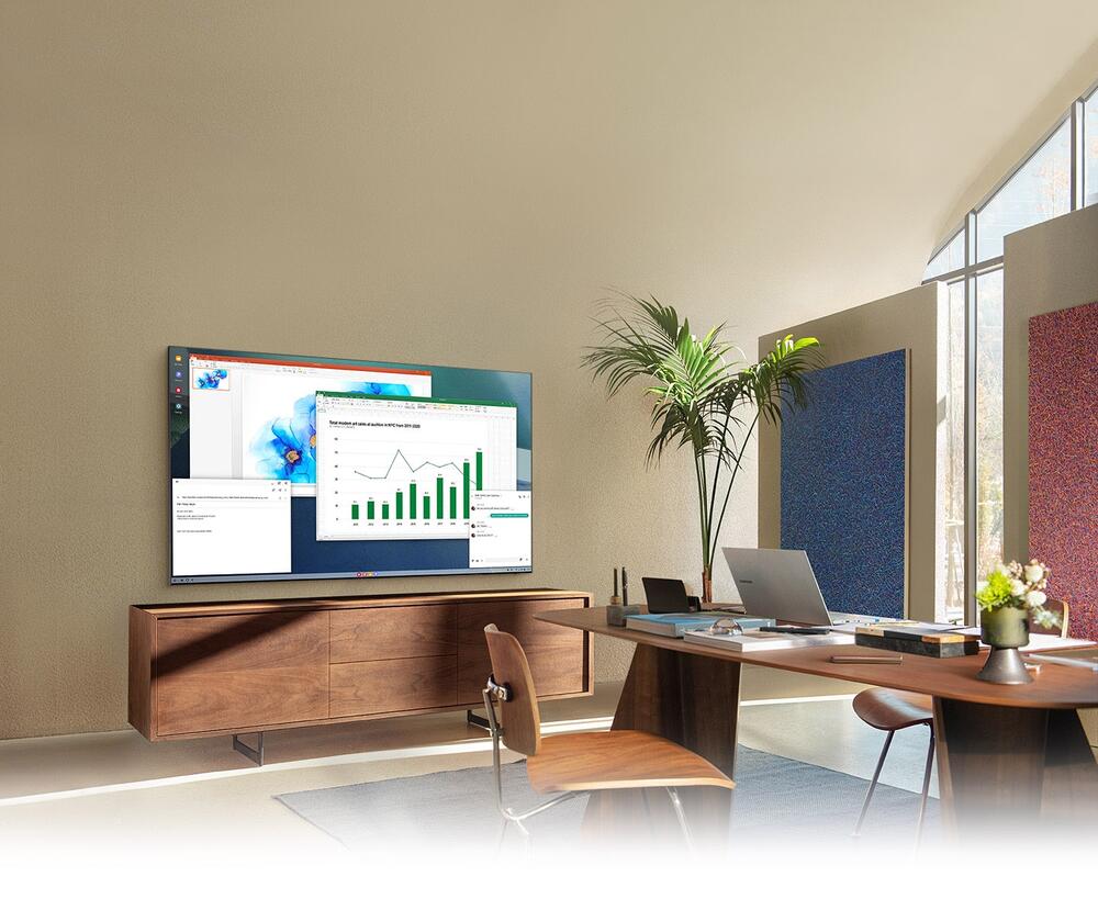 Intr-un birou la domiciliu, ecranul televizorului QLED arata functia PC pe TV care permite conectarea televizorului de acasa la computerul de birou.